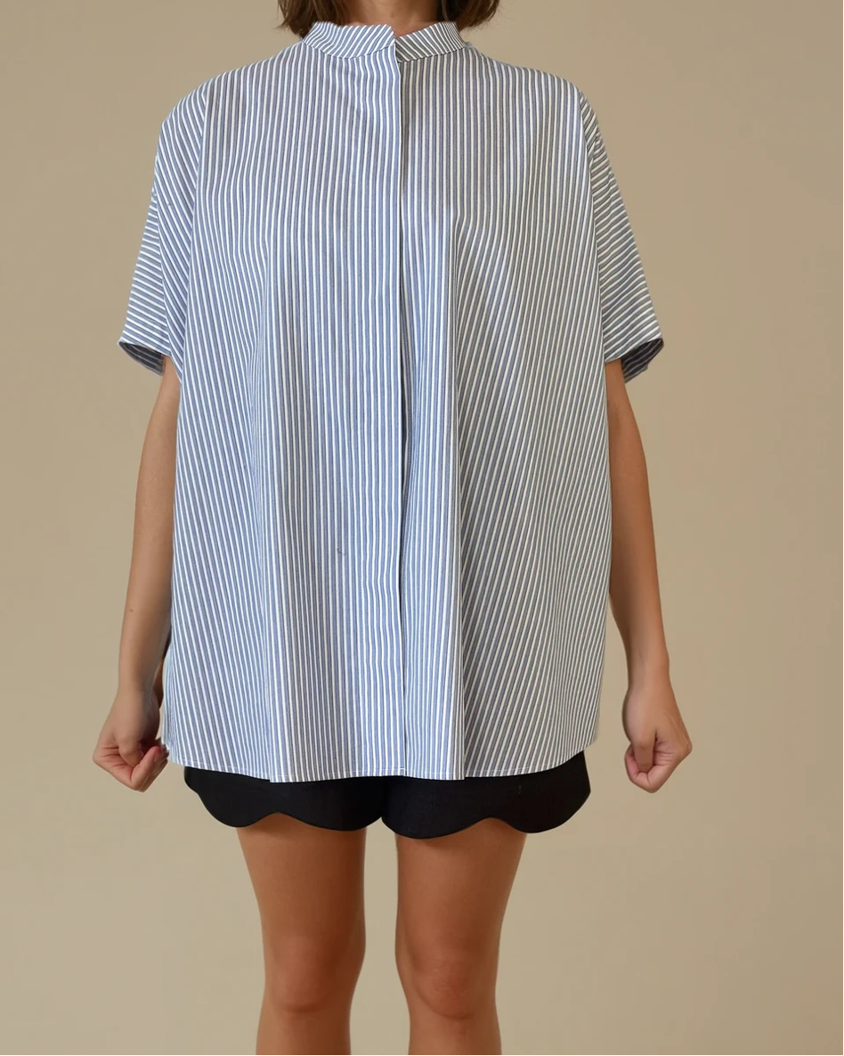 Person wearing a blue and white striped shirt with black shorts on a beige background